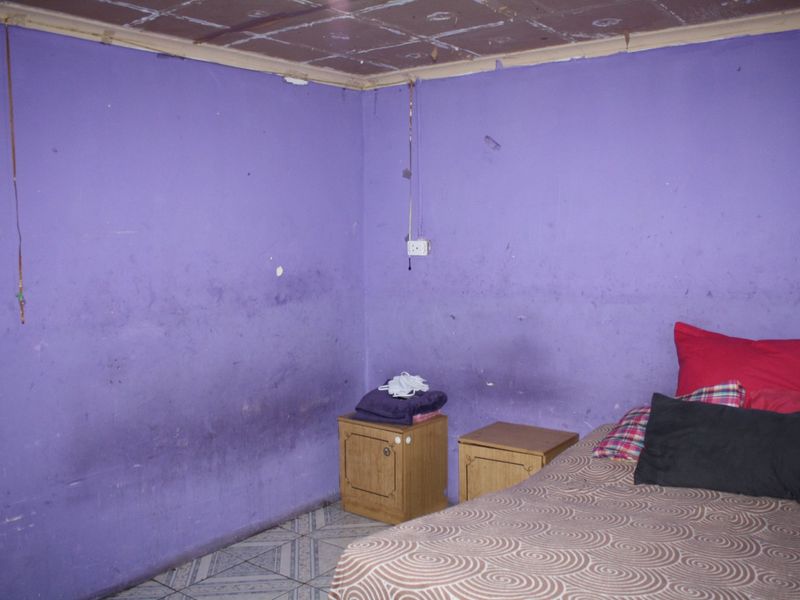 A bedroom featuring tiled flooring and a tiled ceiling, currently requiring significant cosmetic updates and wall repairs.