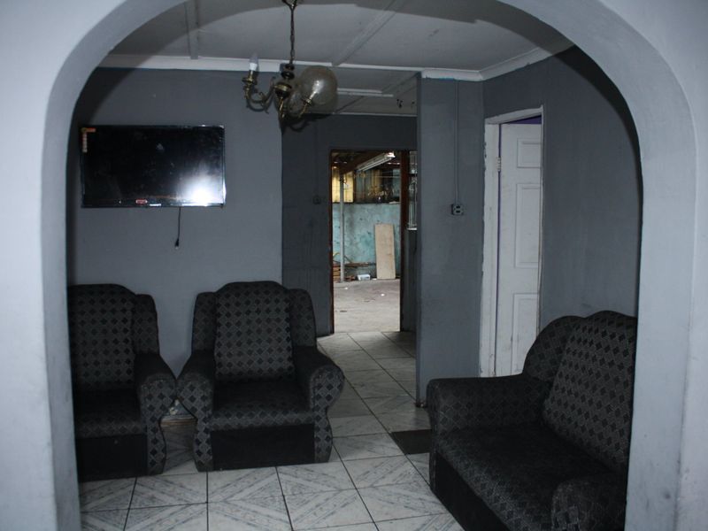 A living room area featuring tiled flooring and an arched entryway, showing signs of wear and requiring cosmetic updates.