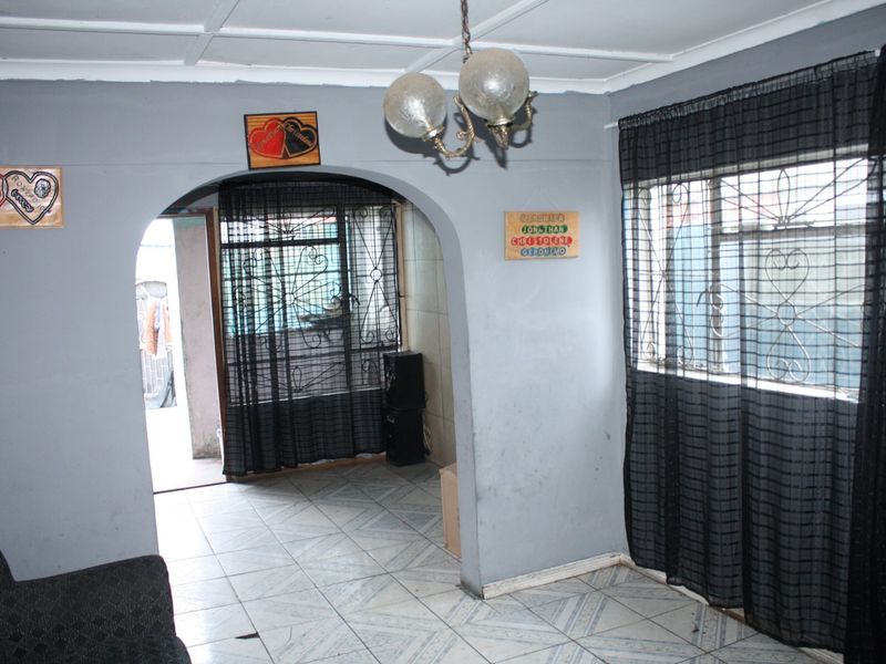 Living room featuring tiled flooring, an arched entryway, and windows fitted with security bars, offering a functional layout with potential for cosmetic updates.