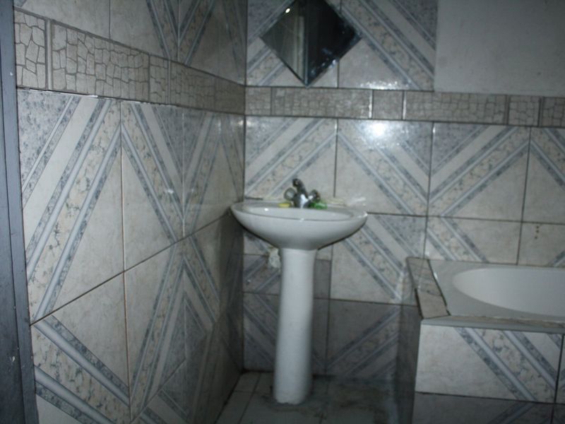 A dated bathroom featuring a pedestal basin and a built-in bathtub with patterned ceramic wall tiles.