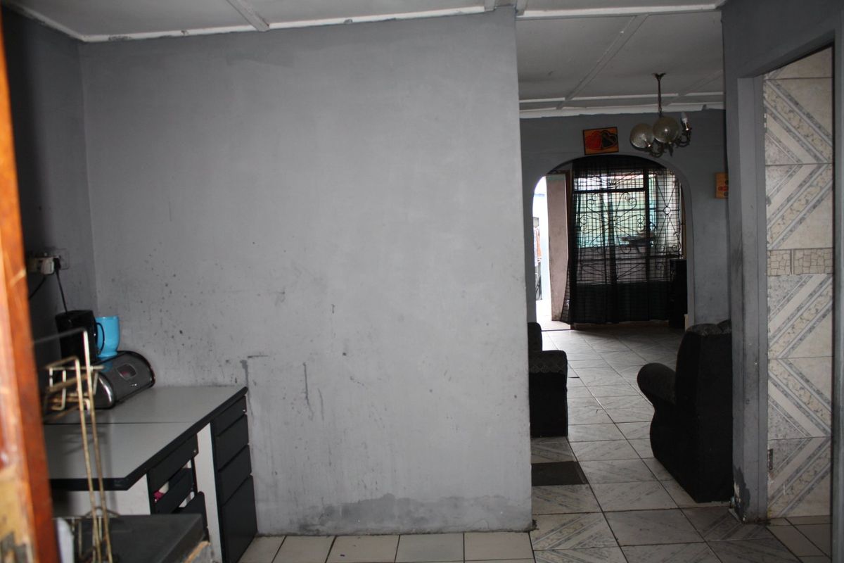 Interior view of a living area featuring tiled flooring and an arched entryway, showing signs of wear on the walls and ceiling.