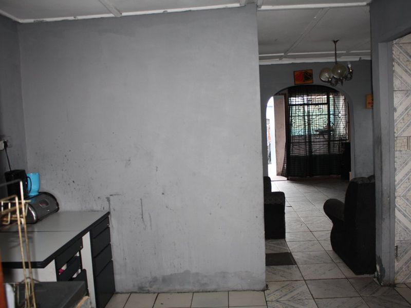 Interior view of a living area featuring tiled flooring and an arched entryway, showing signs of wear on the walls and ceiling.