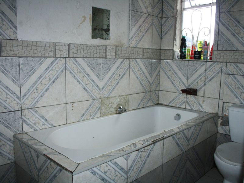 A dated bathroom featuring a built-in bathtub and ceramic wall tiling, requiring renovation and cosmetic updates to improve its overall condition and appeal.