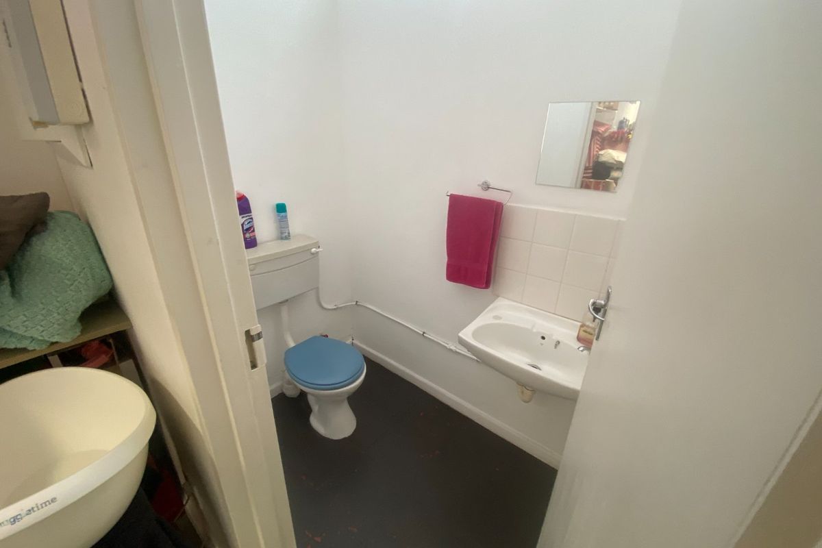 A compact commercial bathroom featuring a wall-mounted basin, toilet, and tiled splashback, requiring minor cosmetic updates to improve the overall finish.