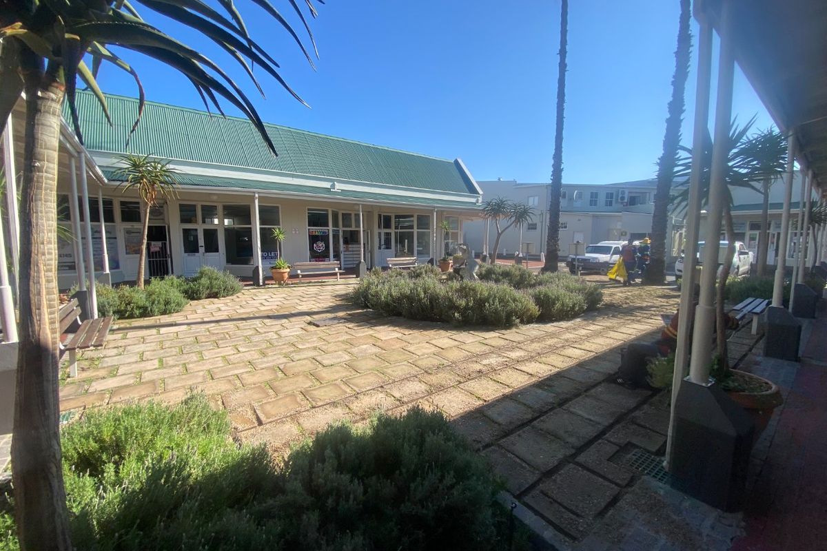 A commercial courtyard featuring a paved central area, landscaped garden beds, and covered walkways providing access to the building units.