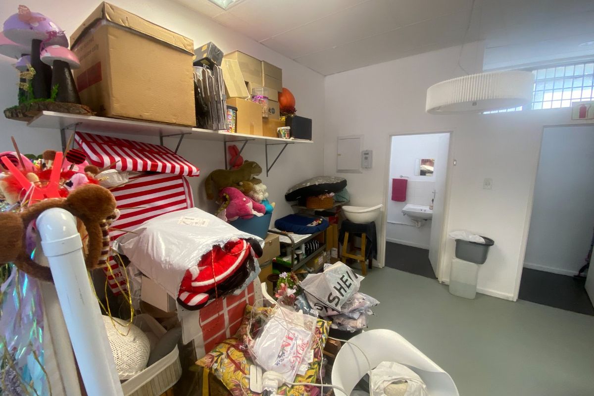 A utility or storage area featuring vinyl flooring, suspended ceiling, and wall-mounted shelving, with an adjacent small washroom visible through the doorway.