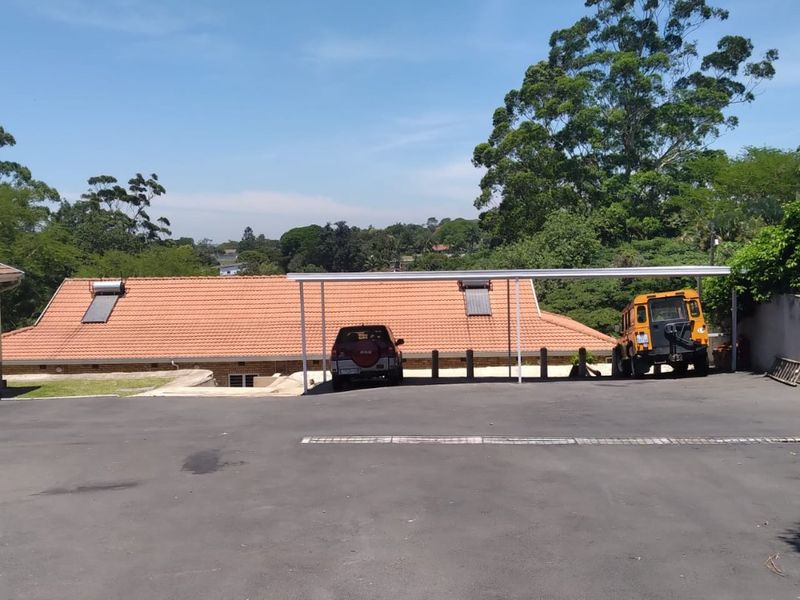 Exterior view of the property featuring a paved driveway, a covered carport structure, and a tiled roof with integrated solar water heating panels.