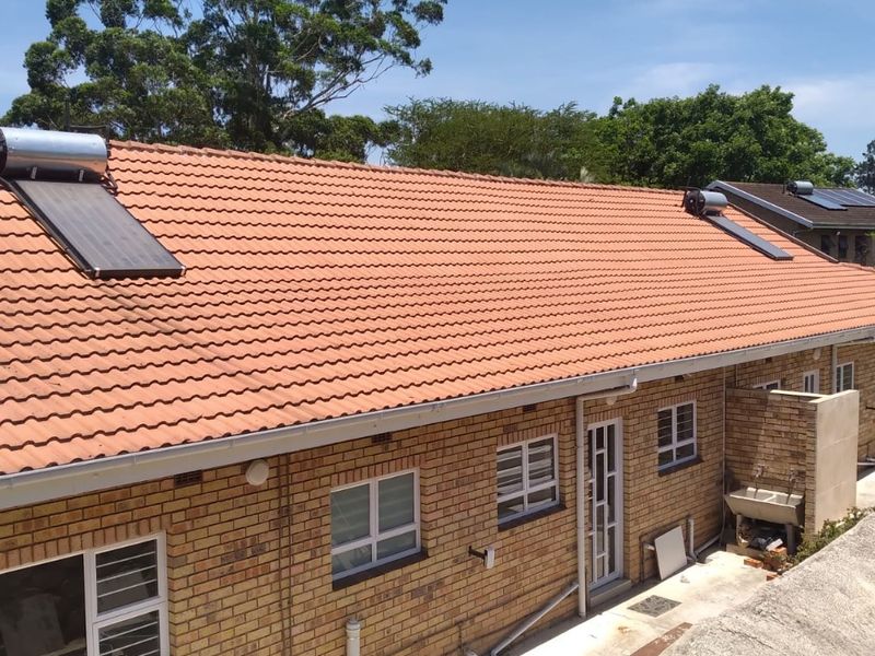 Rear view of a face brick townhouse featuring a tiled roof with integrated solar water heating panels and an external utility sink area.