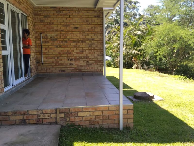 A covered brick patio featuring tiled flooring and sliding glass door access, overlooking a spacious green garden area.