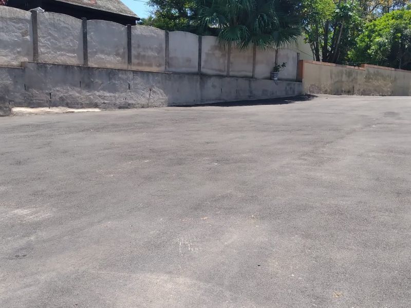 A paved outdoor area featuring a concrete boundary wall and retaining wall, providing a functional space for parking or exterior use.