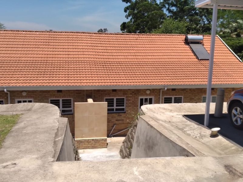Rear view of a facebrick townhouse featuring a terracotta tiled roof, solar water heating system, and concrete retaining walls with an adjacent carport.