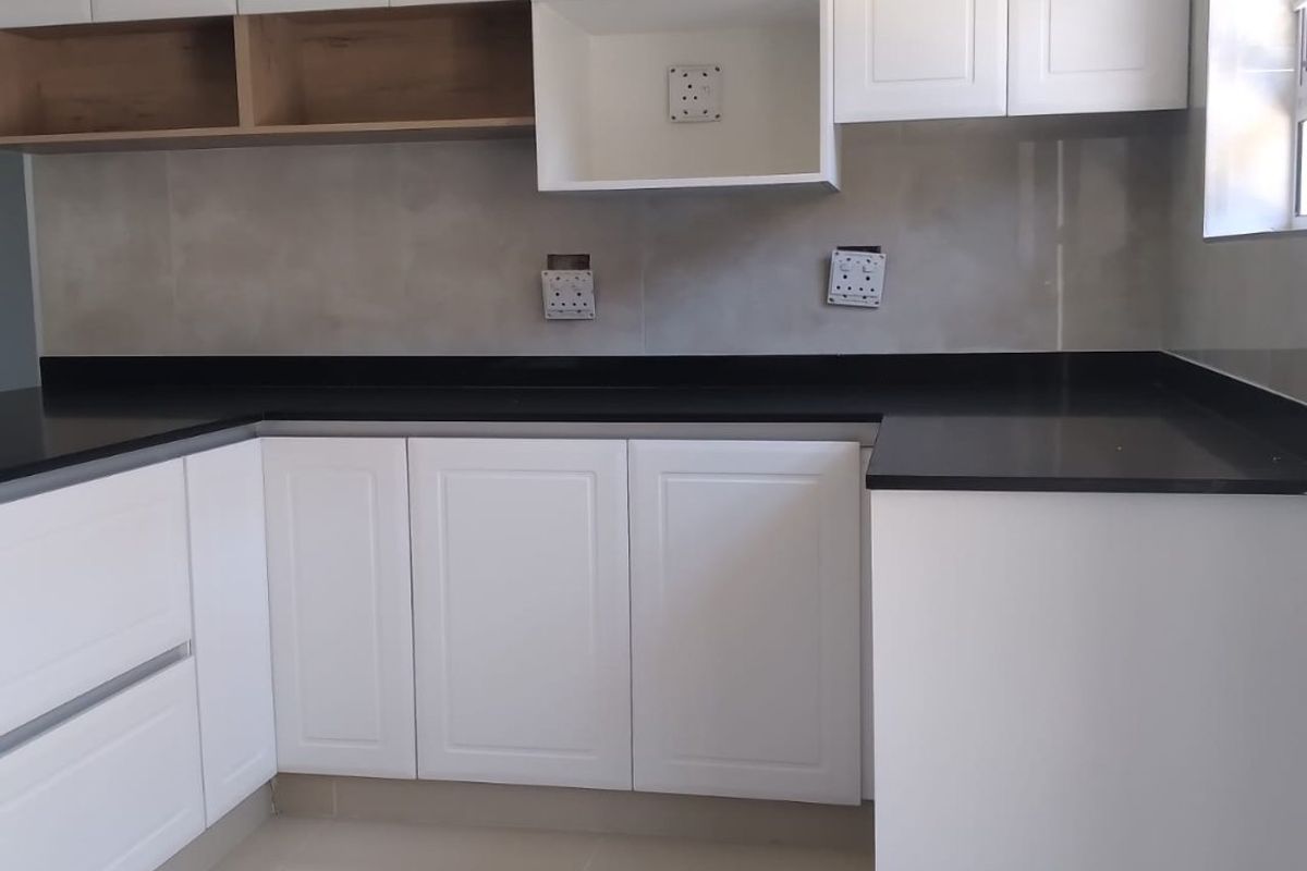 A modern, clean kitchen featuring white shaker-style cabinetry, contrasting black stone countertops, and a neutral tiled backsplash with integrated open shelving.