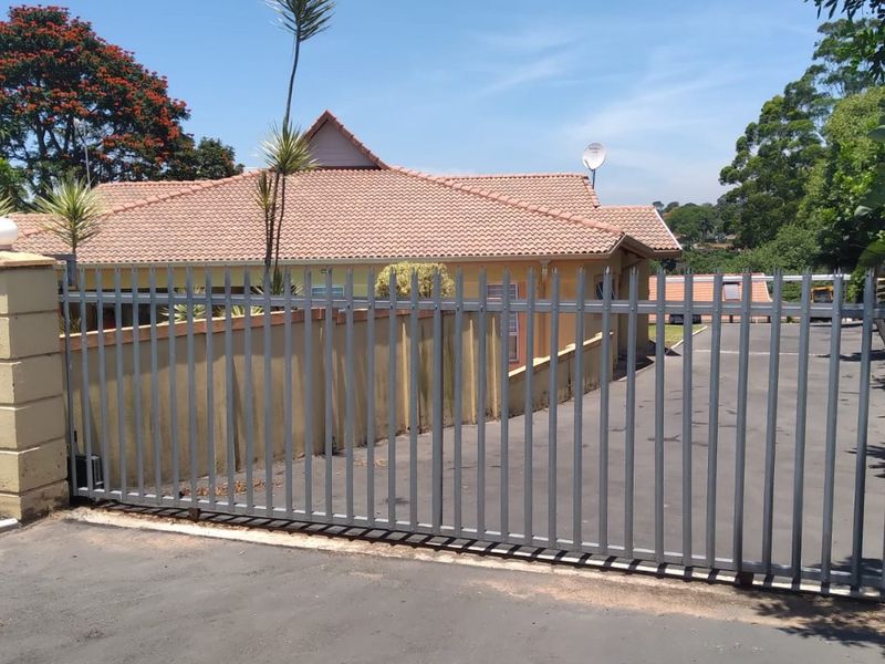 Front view of the townhouse featuring a secure metal gate, paved driveway, and a well-maintained tiled roof structure.