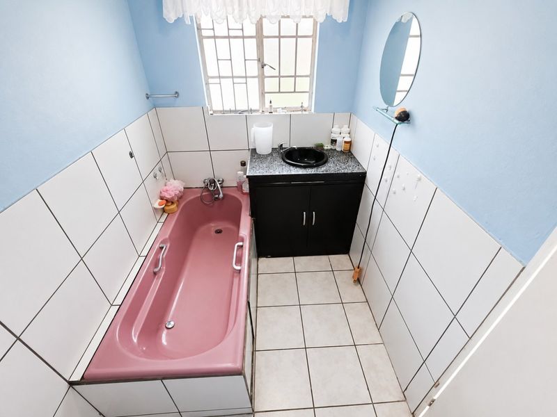 A functional bathroom featuring a pink bathtub, a dark vanity with a basin, and white wall tiling.