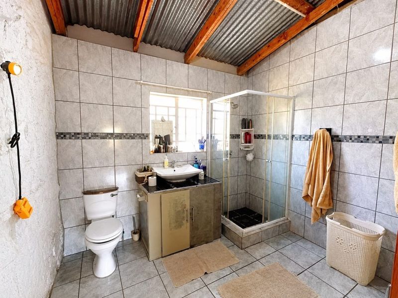 Functional bathroom featuring a shower enclosure, vanity basin, and toilet, with tiled finishes and exposed timber roof rafters.