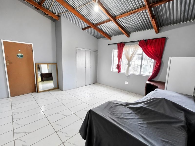 A bedroom featuring tiled flooring, built-in cupboards, and an exposed timber rafter ceiling with corrugated metal roofing.