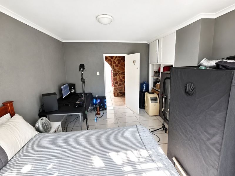 A bedroom featuring tiled flooring, built-in storage cupboards, and a neutral grey wall finish, providing a functional space with direct access to an adjacent room.