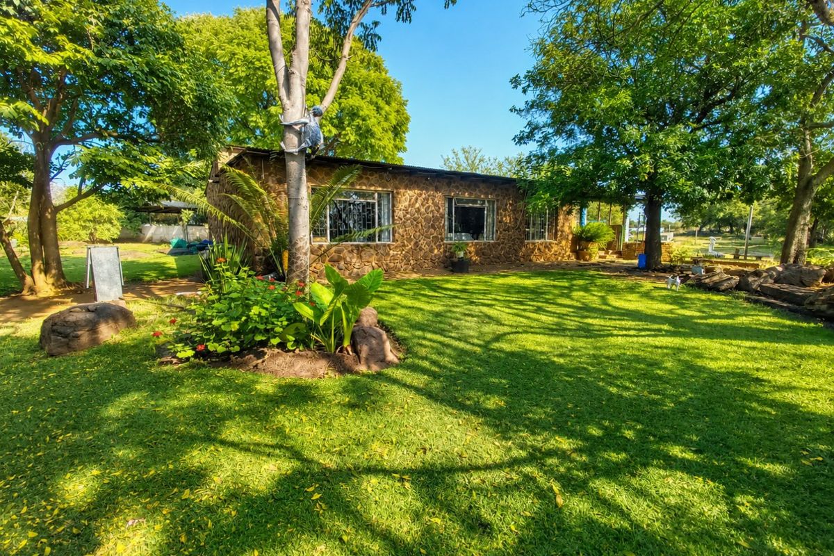 A charming single-story farmhouse featuring natural stone cladding, a metal roof, and security-barred windows, set within a lush, well-maintained garden.
