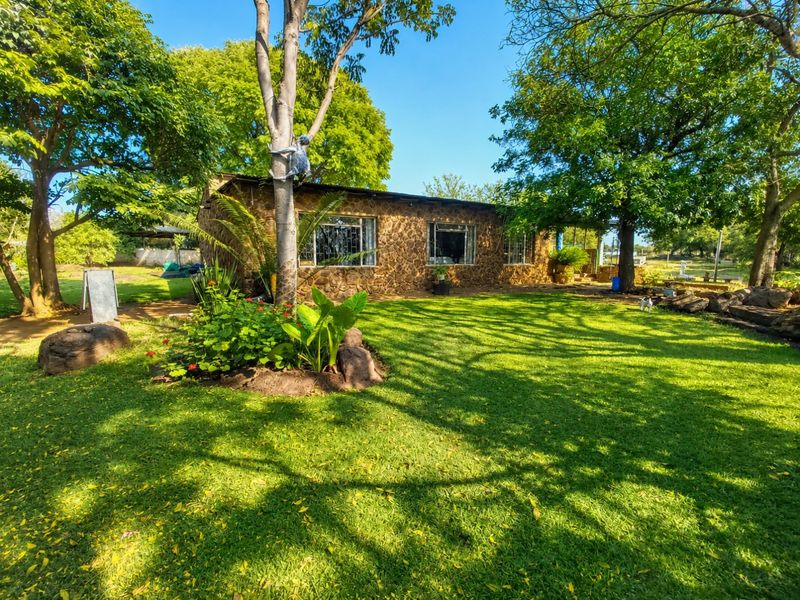 A charming single-story farmhouse featuring natural stone cladding, a metal roof, and security-barred windows, set within a lush, well-maintained garden.