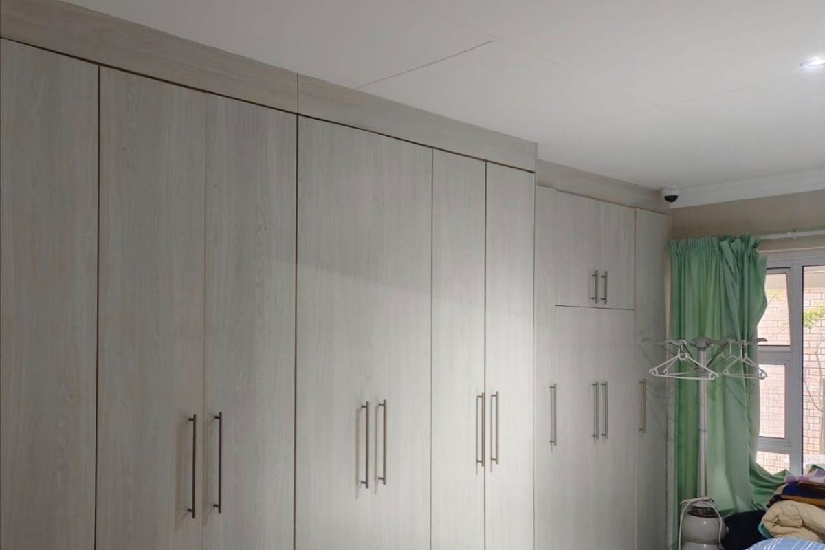 A bedroom featuring extensive light wood-grain built-in cupboards providing ample storage space, complemented by recessed ceiling lighting.