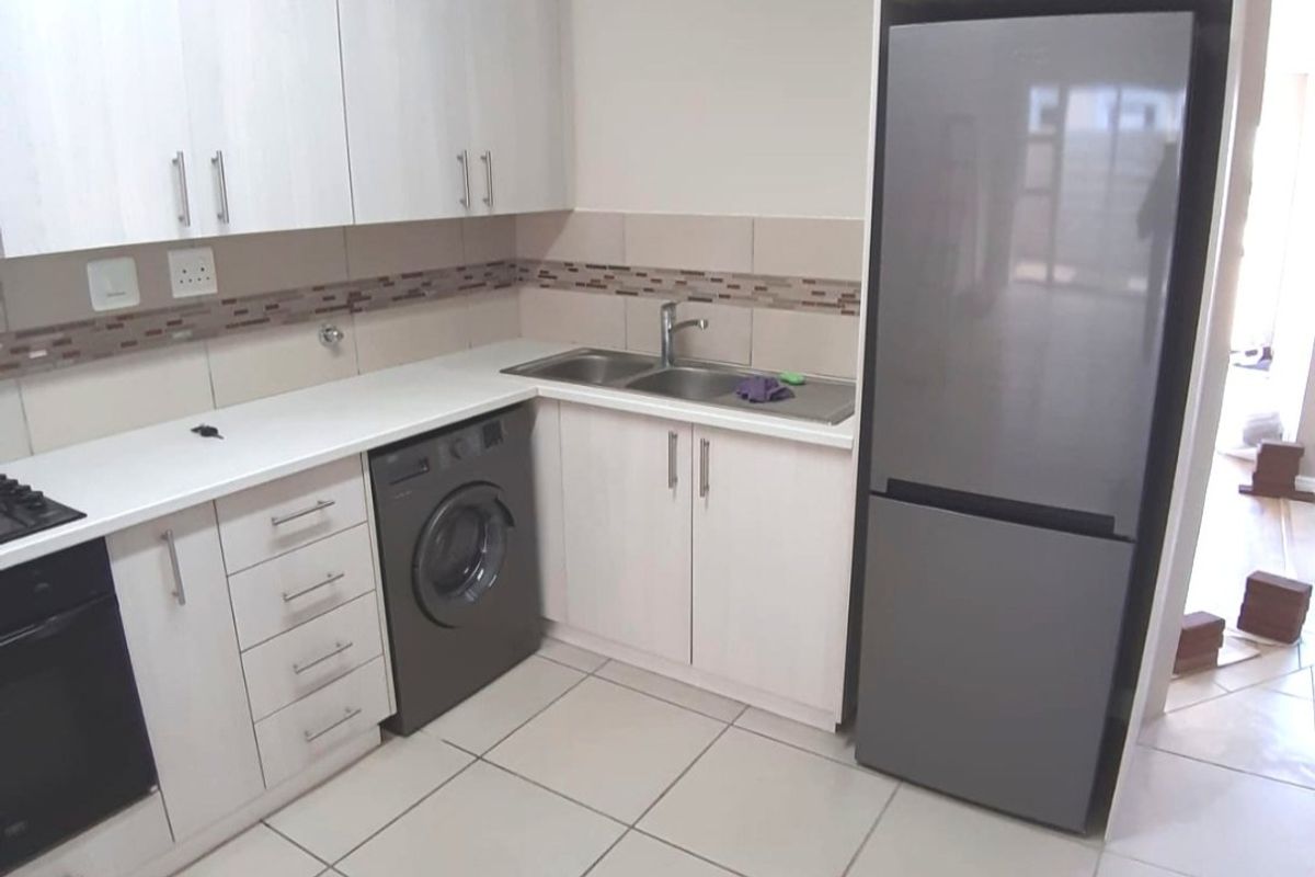 A functional kitchen featuring white cabinetry, laminate countertops, a stainless steel double sink, and built-in oven with tiled flooring.