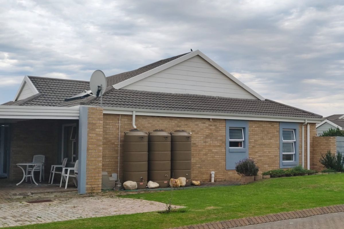 Rear view of a brick house featuring a covered patio, tiled roof, and multiple water storage tanks installed against the exterior wall.