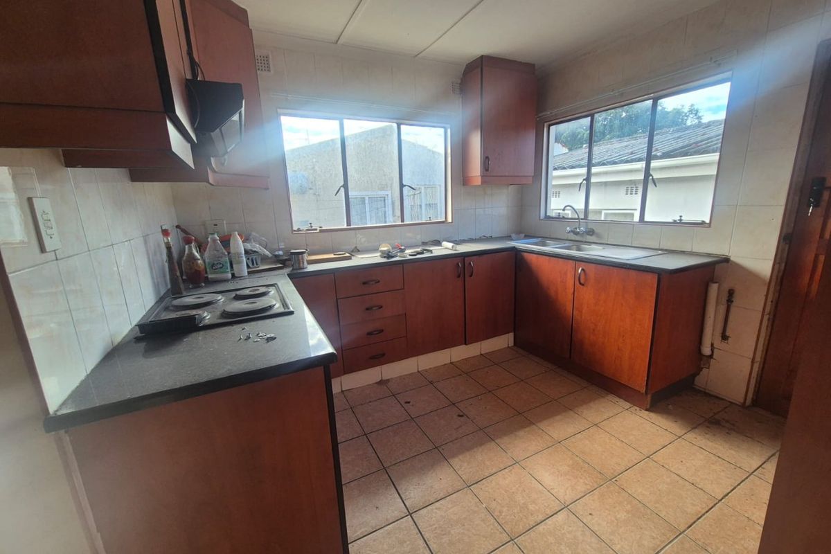 A dated kitchen featuring original laminate cabinetry, electric hob, and tiled flooring, offering significant potential for a modern renovation.