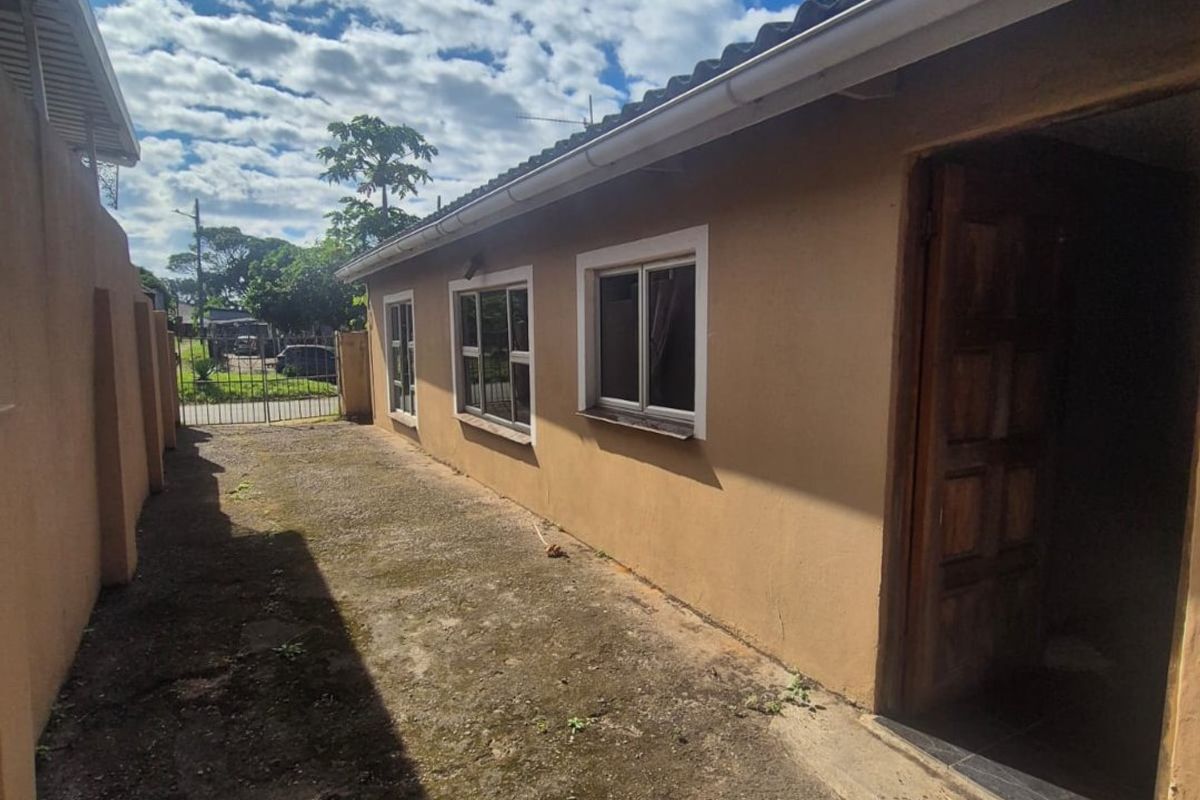A view of the rear exterior side passage featuring concrete paving, boundary walls, and access to the main dwelling.