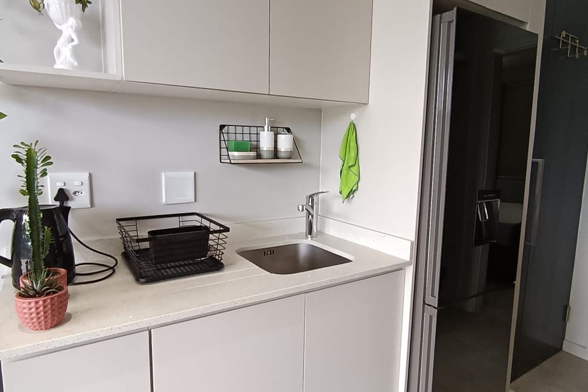 A modern, compact kitchen area featuring sleek handleless cabinetry, stone countertops, an undermount sink, and an integrated refrigerator.