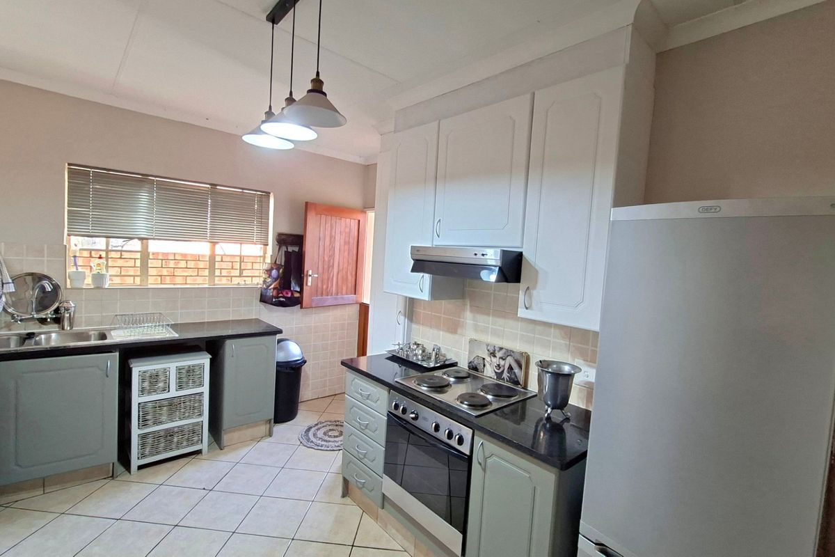Functional kitchen featuring built-in cabinetry, dark countertops, integrated oven and hob, extractor fan, and tiled flooring with direct access to the exterior.