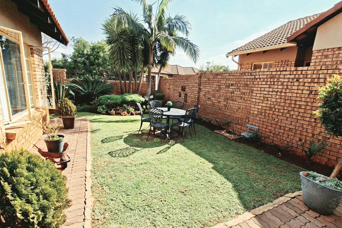 A private rear garden featuring a well-maintained lawn, brick boundary walls, and a paved walkway adjacent to the townhouse structure.