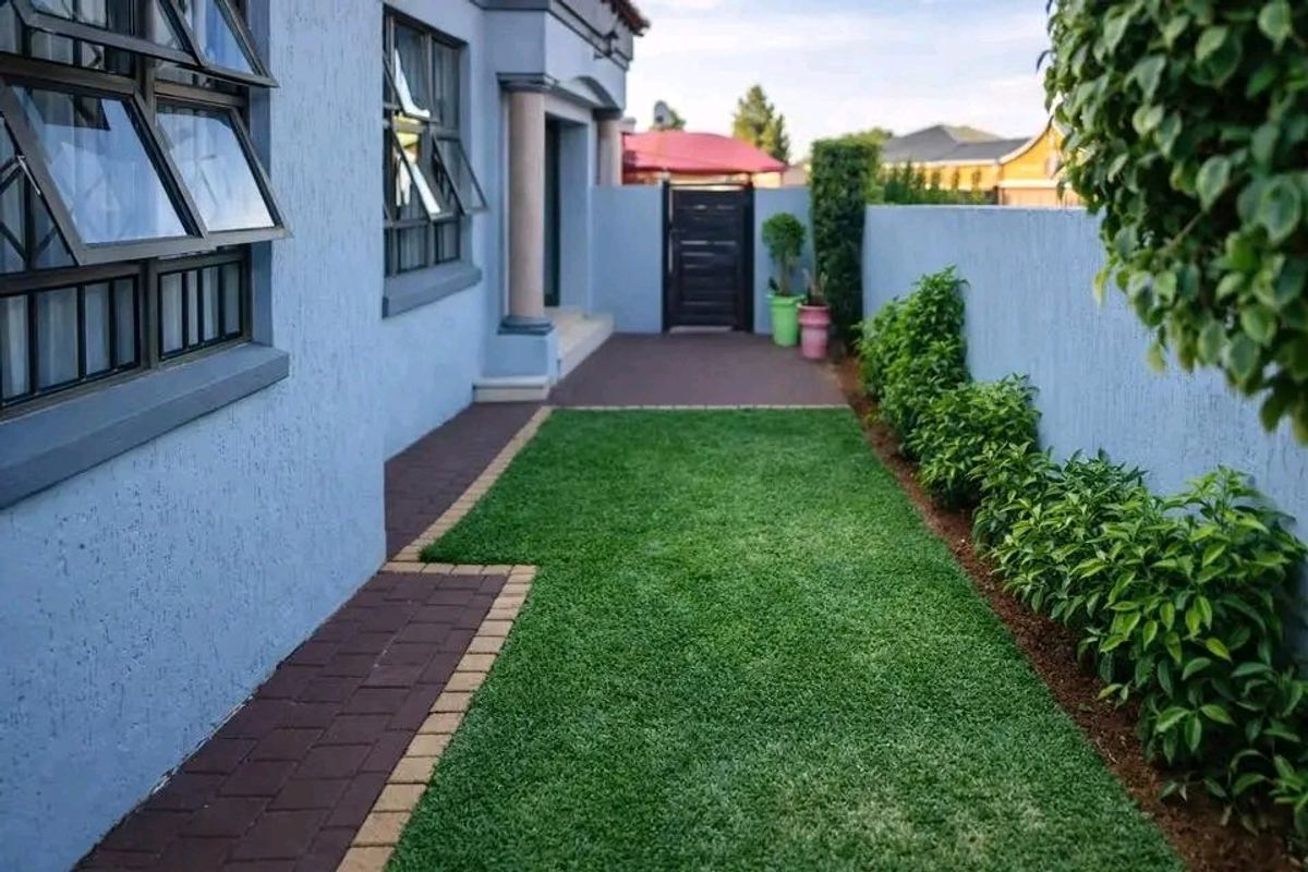 A well-maintained rear garden area featuring a paved walkway, manicured lawn, and secure boundary wall with access gate.