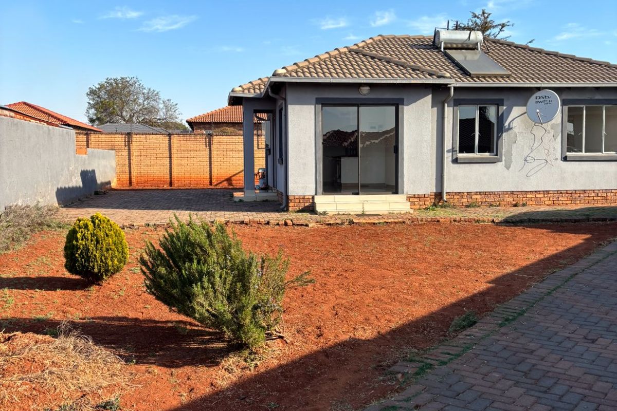 Rear view of a townhouse featuring a paved patio area, solar water heating system, and a large garden space with brick boundary walls.