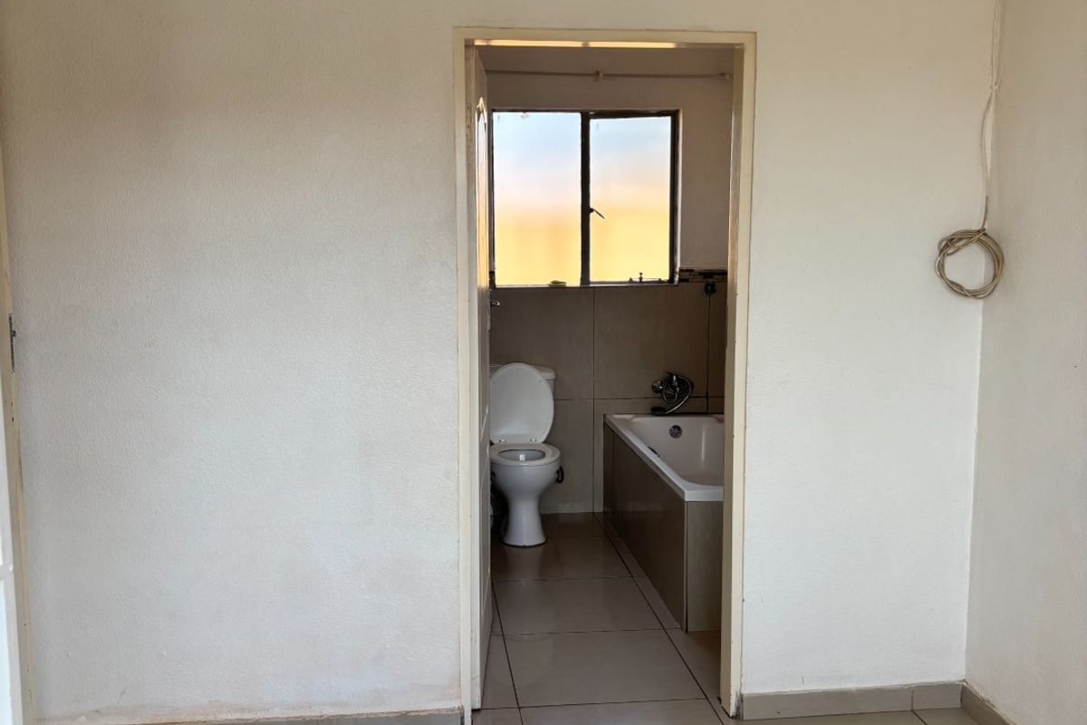 A basic, empty bathroom featuring tiled flooring, a standard bathtub, and a toilet, requiring cosmetic updates and attention to exposed wiring.
