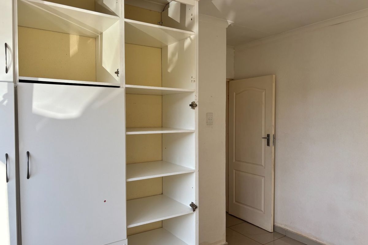 A bedroom featuring built-in shelving units and tiled flooring, currently vacant and in need of minor cosmetic updates.