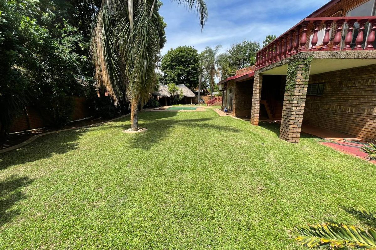 Spacious rear garden featuring a well-maintained lawn, swimming pool, and a covered patio area with a brick balcony above.