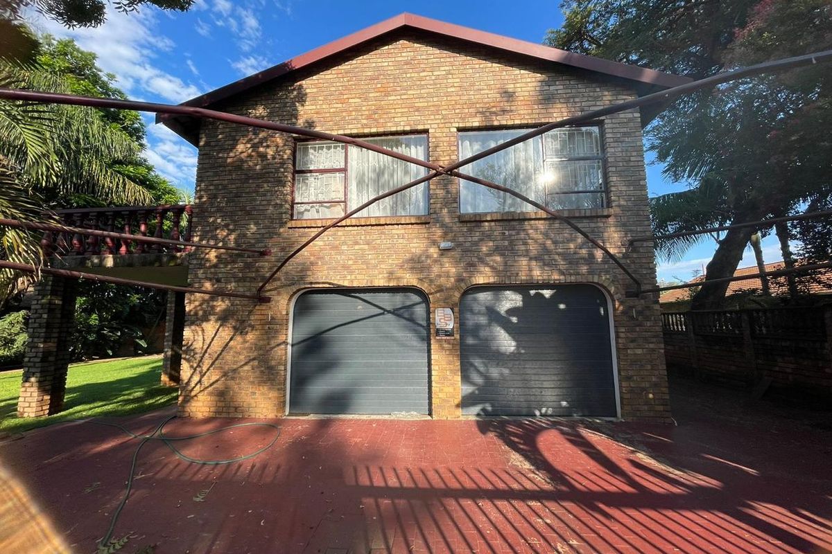 Rear view of a double-story face brick house featuring a double garage, paved driveway, and an elevated balcony with brick balustrades.