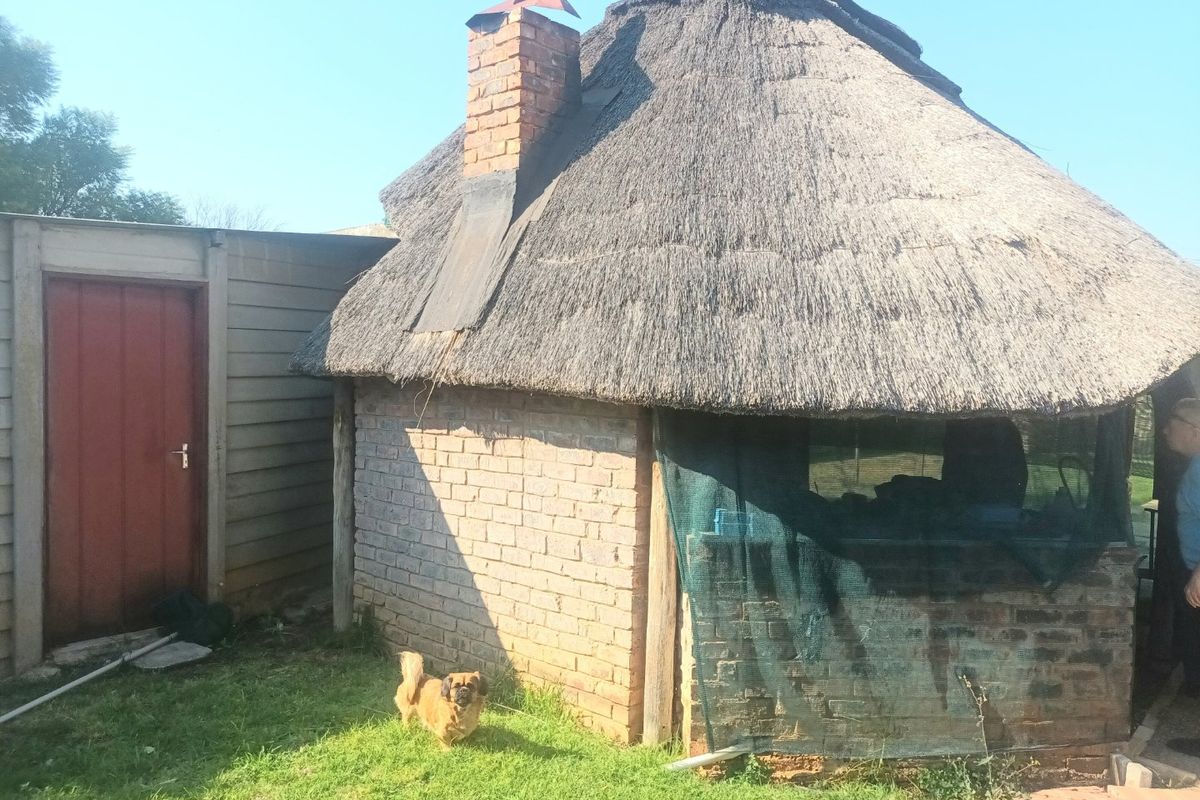 Rear view of a rustic outbuilding featuring a traditional thatch roof, brick chimney, and adjacent side entrance door.