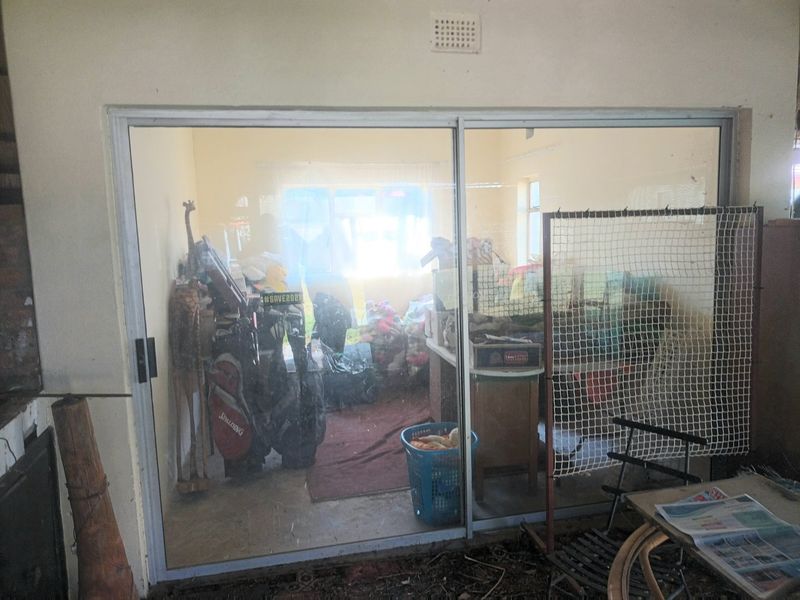 A covered patio area featuring a large sliding glass door looking into an interior room, with visible wear and significant clutter present.