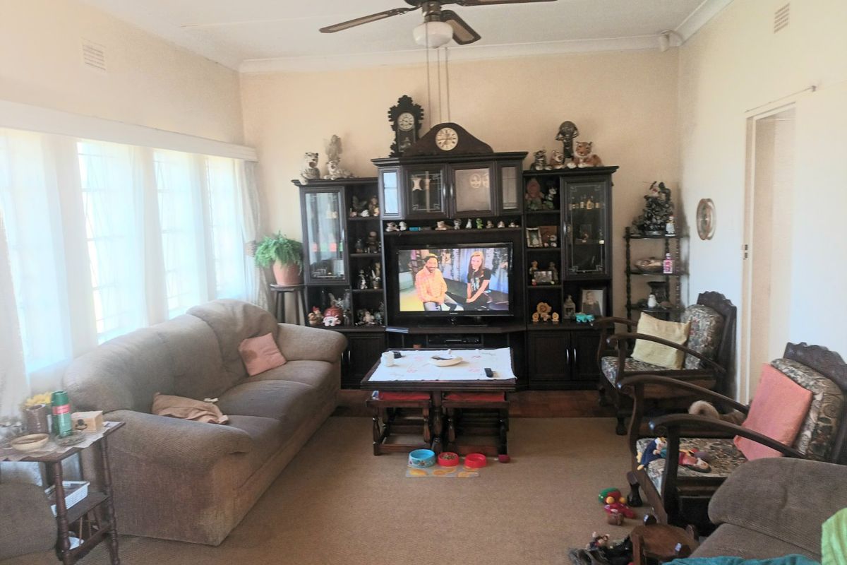 A spacious living room featuring a ceiling fan, large windows allowing natural light, and neutral wall finishes.