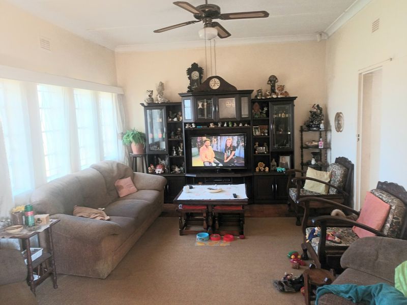 A spacious living room featuring a ceiling fan, large windows allowing natural light, and neutral wall finishes.