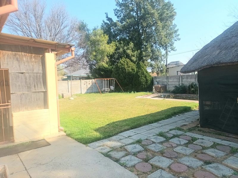 Rear garden area featuring a swimming pool, paved patio, and a thatched lapa structure, enclosed by precast concrete boundary walls.