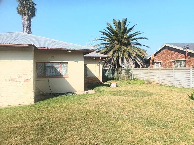 Rear view of the property featuring a lawn, corrugated metal roof, and precast concrete boundary wall.