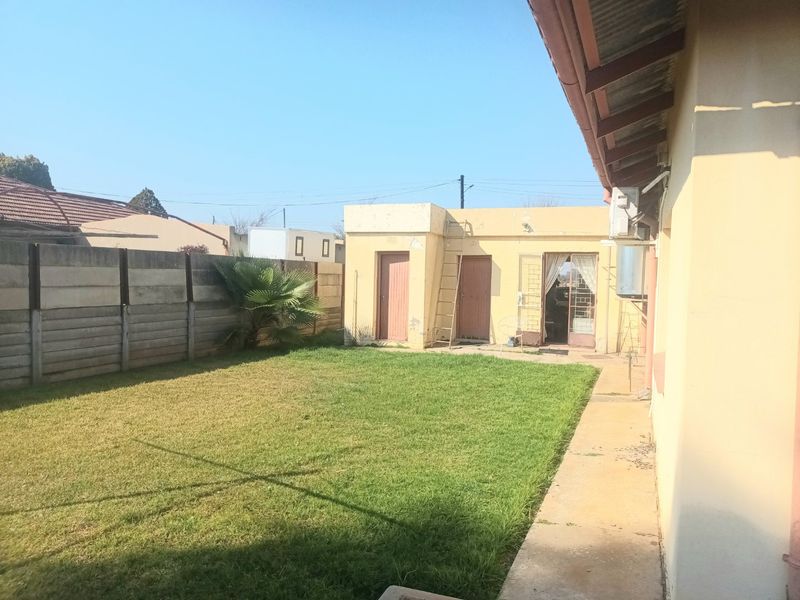 Rear garden area featuring a lawn, precast concrete boundary wall, and a detached outbuilding with visible exterior wear.