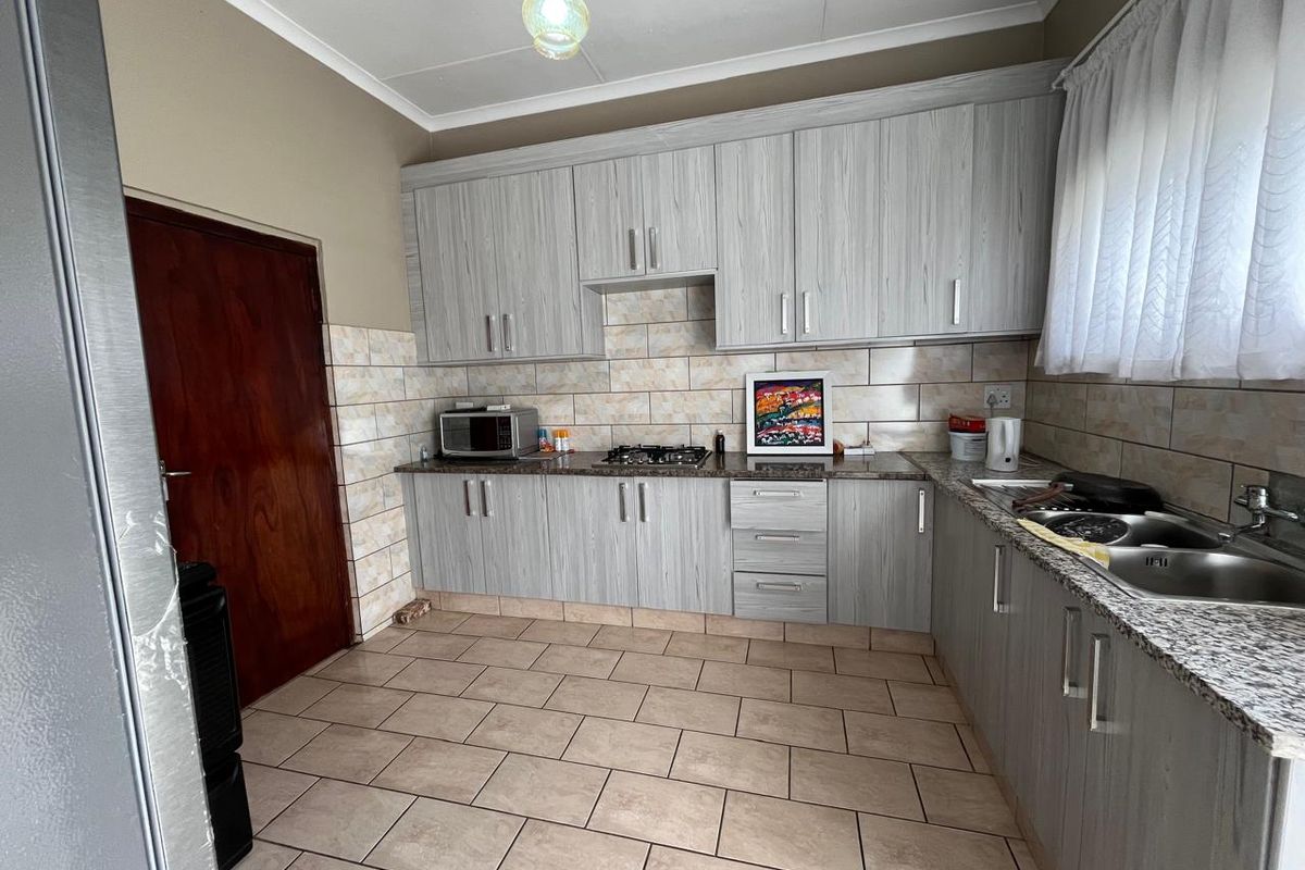Functional kitchen featuring light wood-grain cabinetry, granite countertops, a gas hob, and tiled flooring with a neutral backsplash.