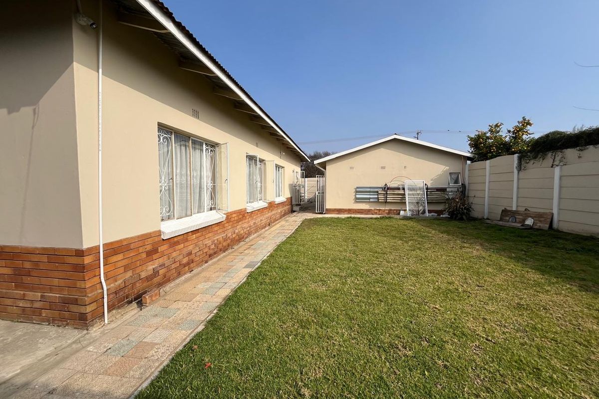 Rear exterior view of the property featuring a brick-accented facade, paved walkway, and a well-maintained lawn enclosed by a precast concrete boundary wall.
