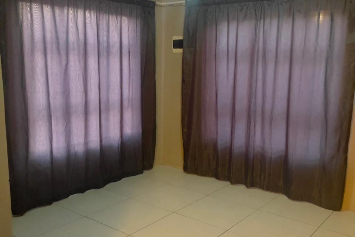 An empty bedroom featuring neutral tiled flooring and dual windows with installed curtain rails.
