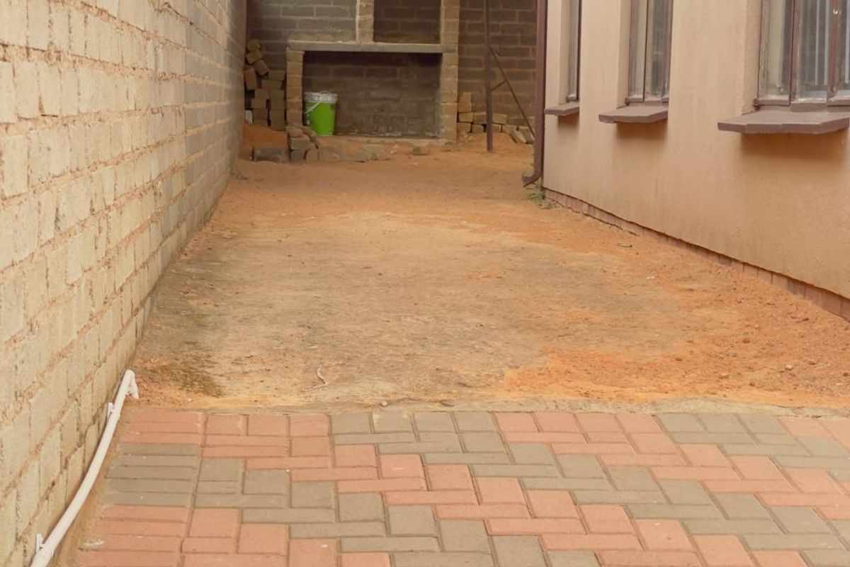 Rear exterior area featuring a built-in braai, paved section, and carport structure, currently requiring landscaping and finishing touches.