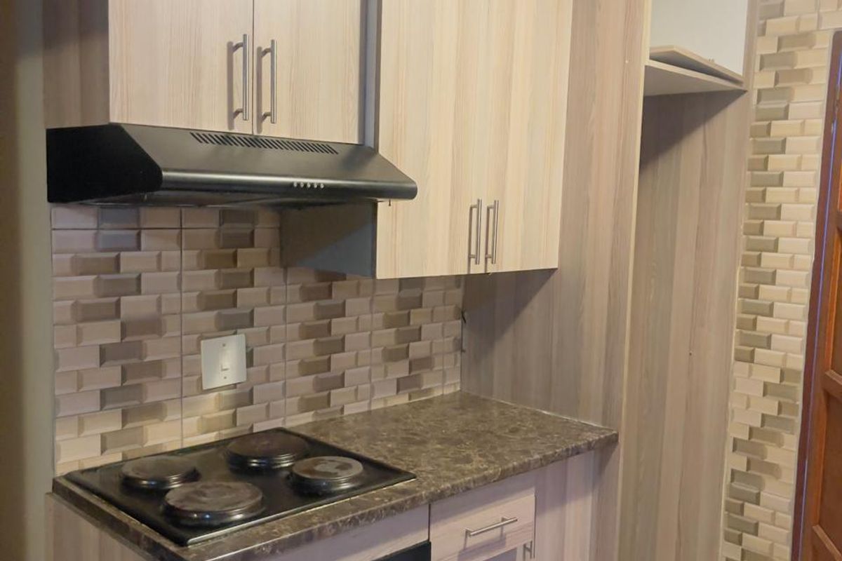 Compact kitchen featuring light wood-finish cabinetry, stone-look laminate countertops, a built-in electric stove with extractor fan, and decorative tiled backsplash.