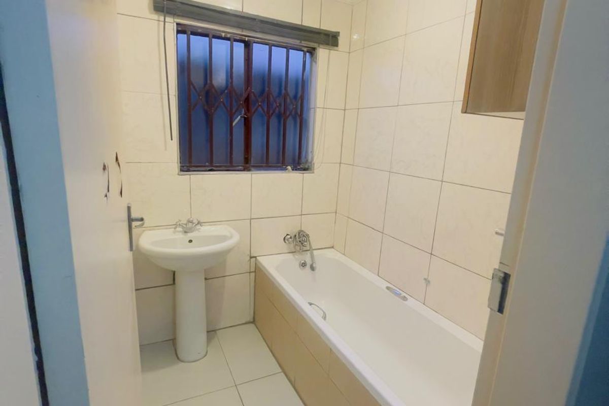 A functional bathroom featuring a pedestal basin, bathtub, and neutral wall and floor tiling, providing a clean and practical space.